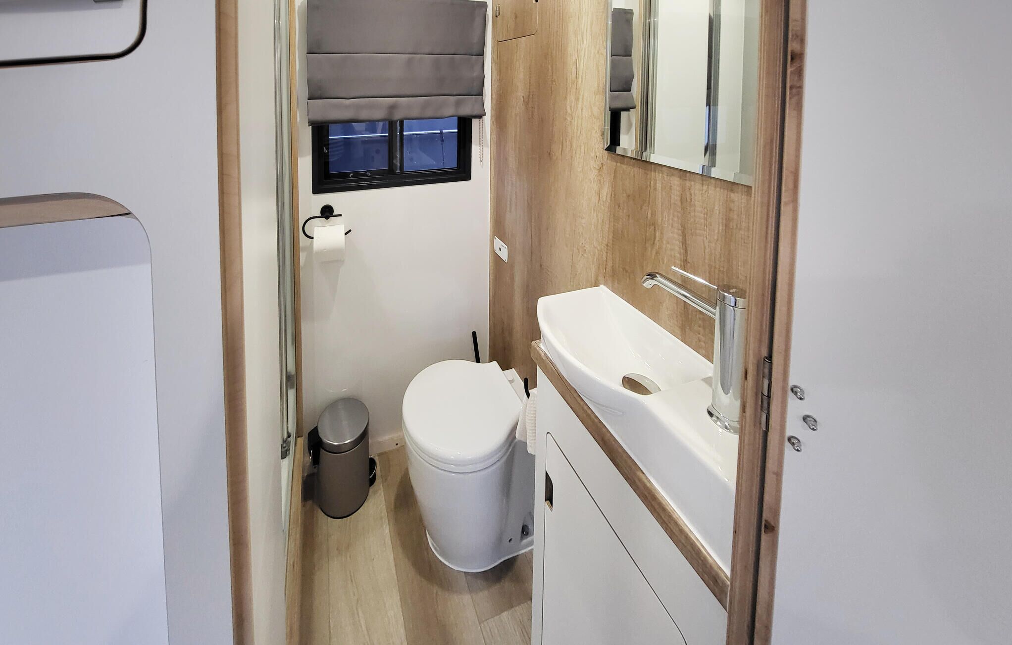 Une petite salle de bain comprenant des toilettes, un lavabo et une fenêtre avec un store.
