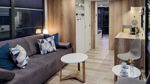 Una sala de estar moderna con un sofá gris, cojines estampados, una mesa de centro redonda y una pequeña mesa de comedor con sillas.