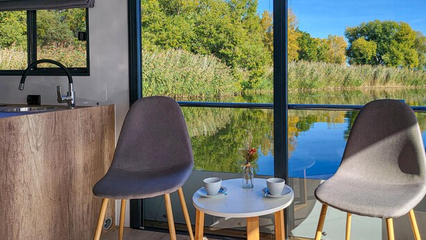 Habitación moderna con un ventanal grande que da a un paisaje natural. Cuenta con una mesa redonda pequeña con dos sillas y un jarrón con flores.
