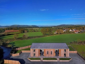 A modern building with a flat roof and a symmetrical facade, surrounded by green fields and distant hills.
