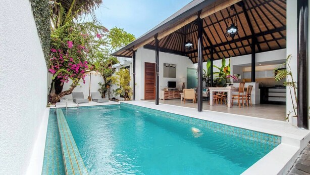 Une piscine avec un patio couvert, un espace repas et une cuisine visible à travers une porte ouverte.