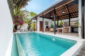 Ein Schwimmbad mit überdachter Terrasse, Essbereich und sichtbarer Küche durch eine offene Tür.