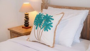 Un lit bien fait, avec du linge de lit blanc et un oreiller orné d’un motif représentant un palmier.