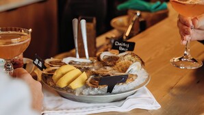A bar area with a wooden counter, a plate of oysters on ice, and a person holding a cocktail glass. - Penny's Motel & Apres (Thornbury)
