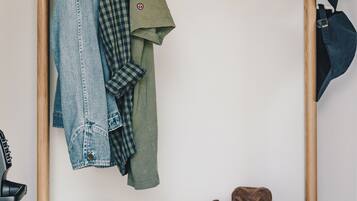 A wooden wardrobe with hanging clothes and a shelf with sunglasses, a hat, and a wallet.