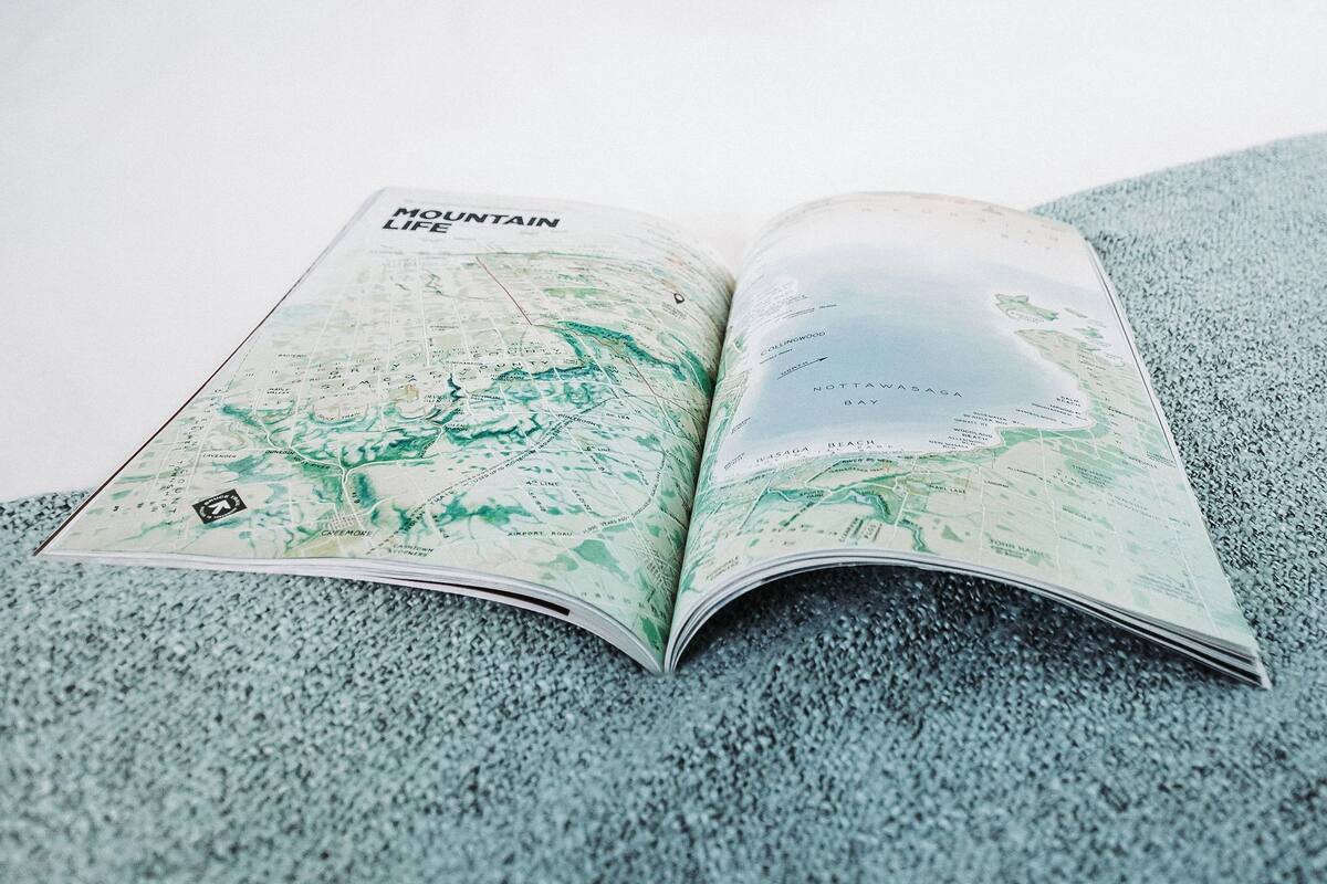 Una cama con un libro de mapas abierto, almohadas y un mural en la pared.