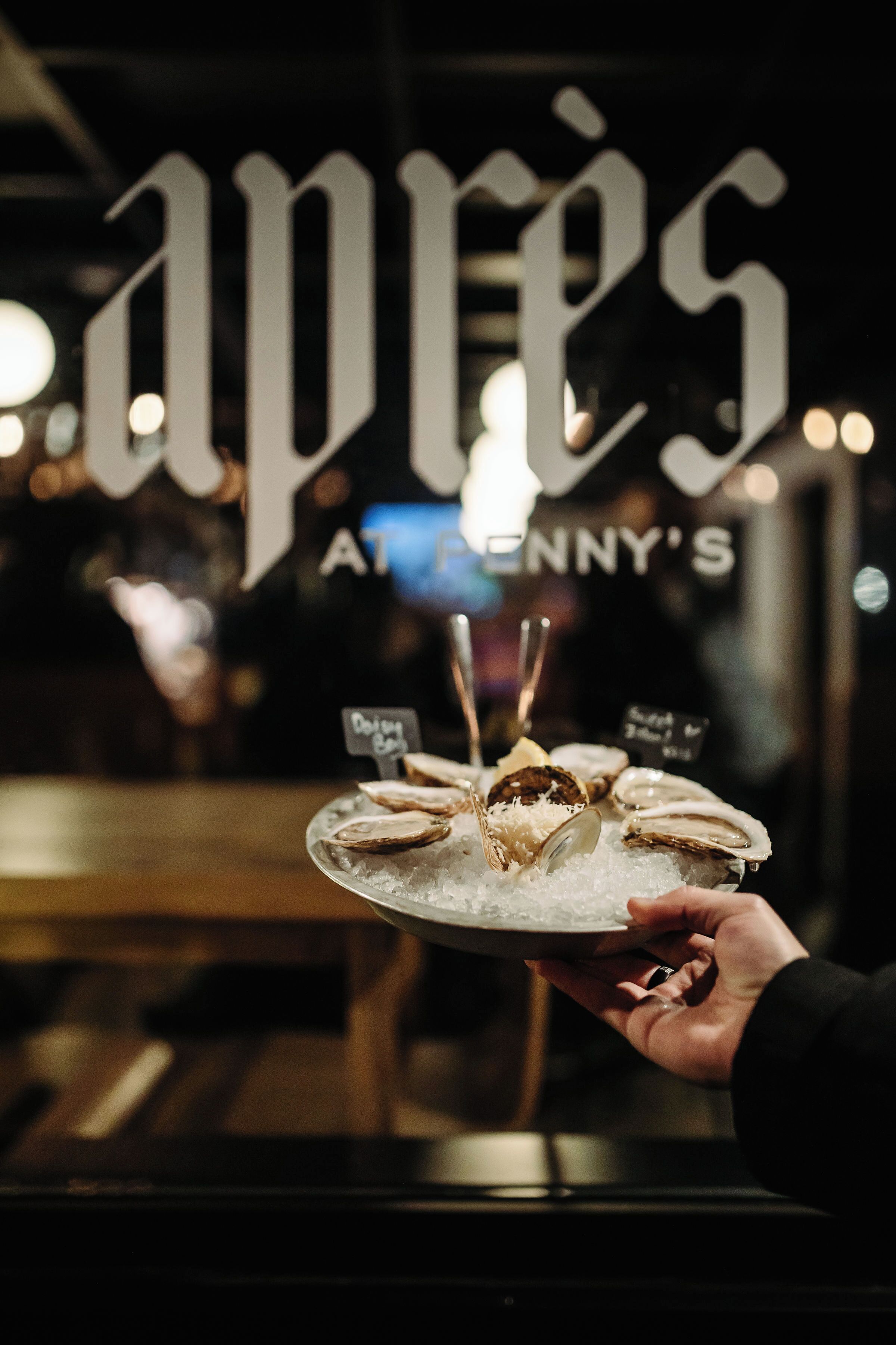 A person holding a plate of oysters on ice with a sign reading "Oyster" in a restaurant.