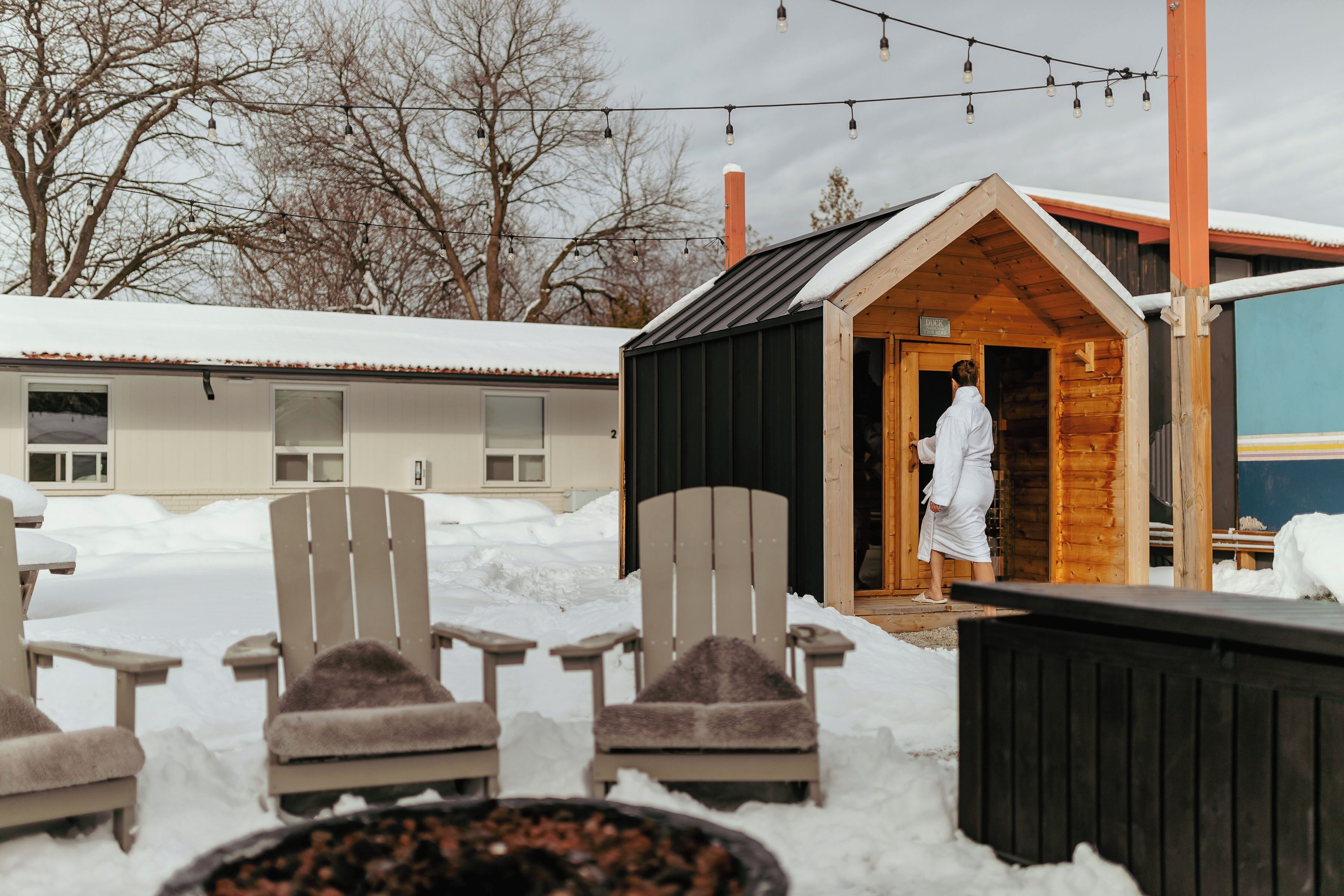 Un espacio al aire libre cubierto de nieve, con sillas de madera y una estructura de sauna.