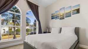 Ein Schlafzimmer mit einem großen Bett, einem Fenster mit Vorhängen und einer Wand mit drei Landschaftsbildern.