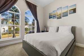 Un dormitorio con una cama grande, una ventana con cortinas y una pared con tres cuadros de paisajes.