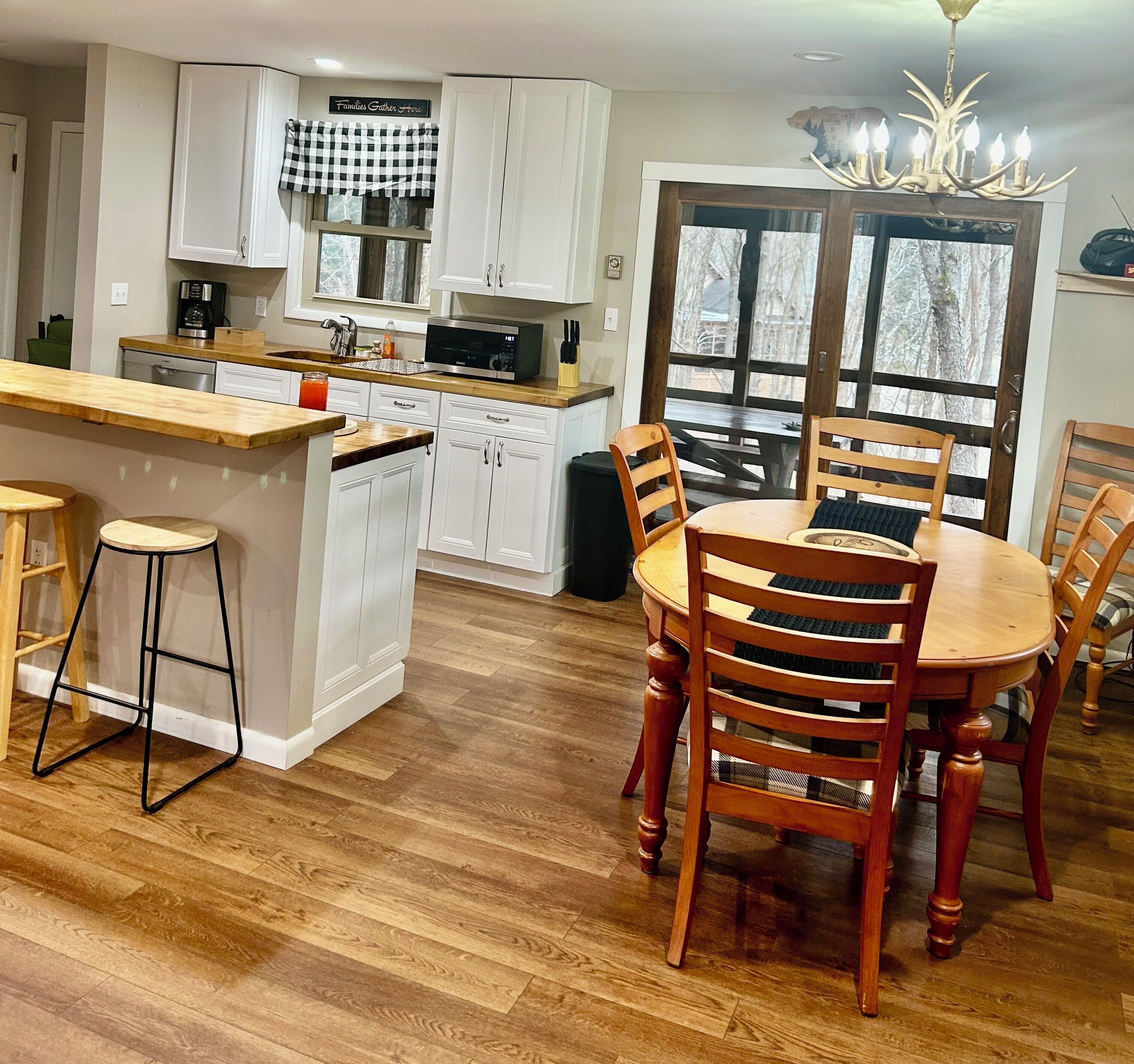 A modern kitchen with white cabinetry, a wooden island with stools, and a dining area with a wooden table and chairs.