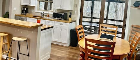 A modern kitchen with white cabinetry, a wooden island with stools, and a dining area with a wooden table and chairs.