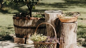 Un entorno rústico al aire libre con una jardinera de árbol, troncos de madera y una cesta de mimbre con flores.