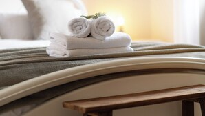 Una cama bien hecha con toallas blancas enrolladas y un taburete de madera pequeño en una habitación de hotel.
