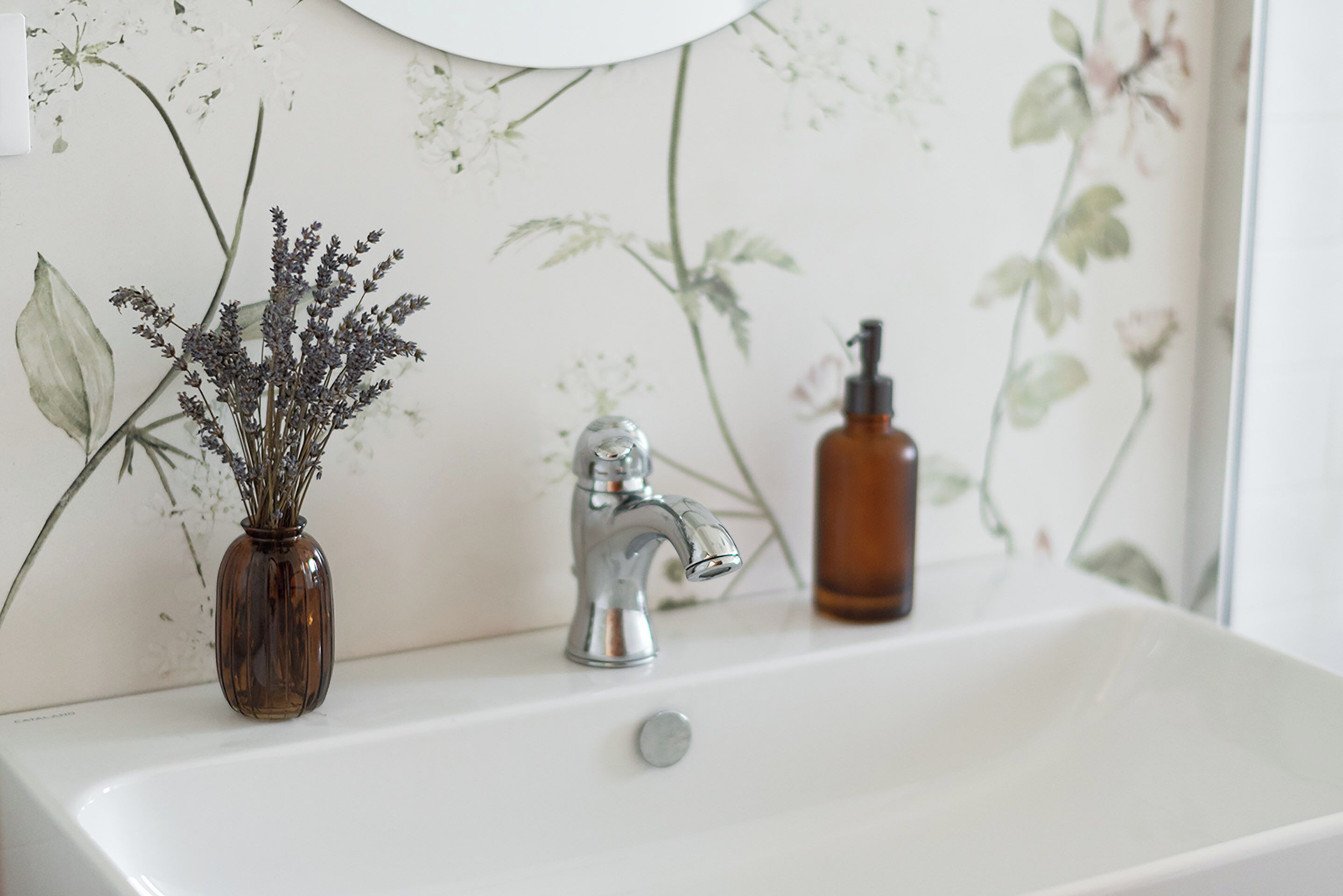 Une salle de bain avec un lavabo blanc, un robinet argenté et une bouteille marron posée sur le comptoir.