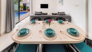 Een eetruimte met een tafel voor zes personen, een bank op de achtergrond en uitzicht op een zwembad.