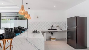Een moderne keuken met een marmeren aanrecht, een zwarte koelkast en rieten hanglampen.