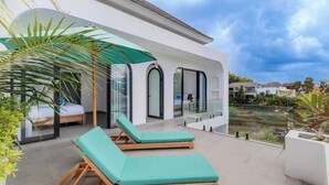 Een moderne villa met een balkon, twee lounge stoelen, een glazen deur en uitzicht op een waterpartij.