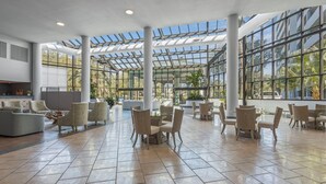 Eine geräumige Lobby mit hoher Decke, großen Fenstern und verschiedenen Sitzbereichen, darunter Sofas und Tische.