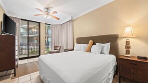 Une chambre d’hôtel avec un lit, un ventilateur de plafond, une télévision, une lampe et une vue sur le balcon extérieur.