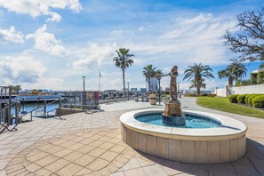 Un espace piscine agrémenté d’une fontaine, de palmiers et offrant une vue sur le port de plaisance.