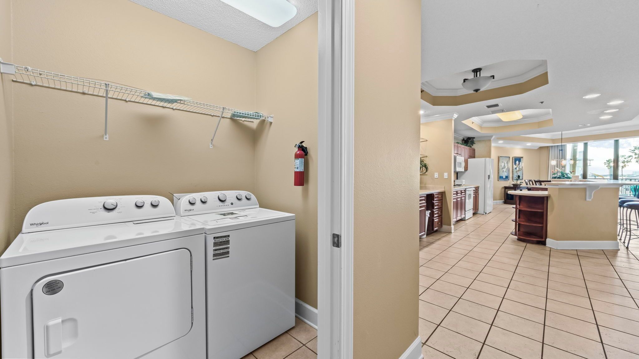 Un'area lavanderia con lavatrice e asciugatrice Whirlpool, un estintore e un'asta per stendere il bucato a soffitto.