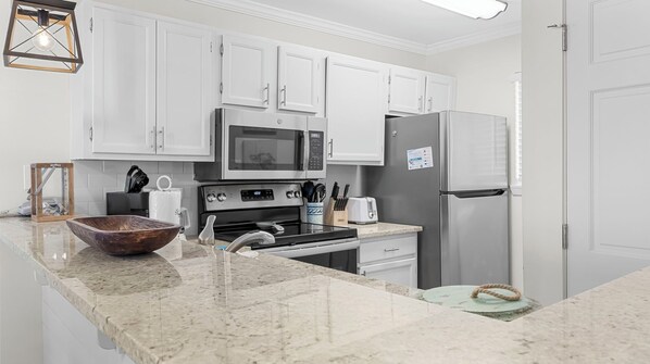A modern kitchen with white cabinets, a stainless steel refrigerator, a microwave, and a stove. - Salt and Light at Romar Beach 213 (Orange Beach)