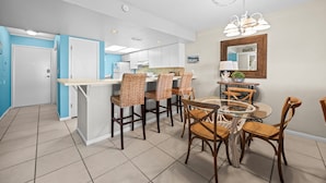 Une cuisine moderne avec des meubles blancs, un îlot central et un coin repas agrémenté de chaises en osier et d’une table en verre.