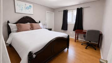 Un dormitorio con una cama, un escritorio, una silla, una ventana con cortinas y una puerta.