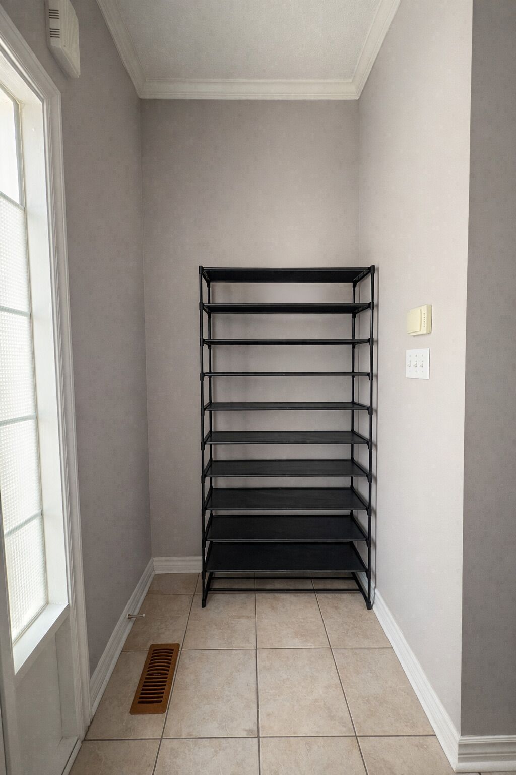 A corner room with a black metal shelf unit against the wall, a window with blinds, and a door.