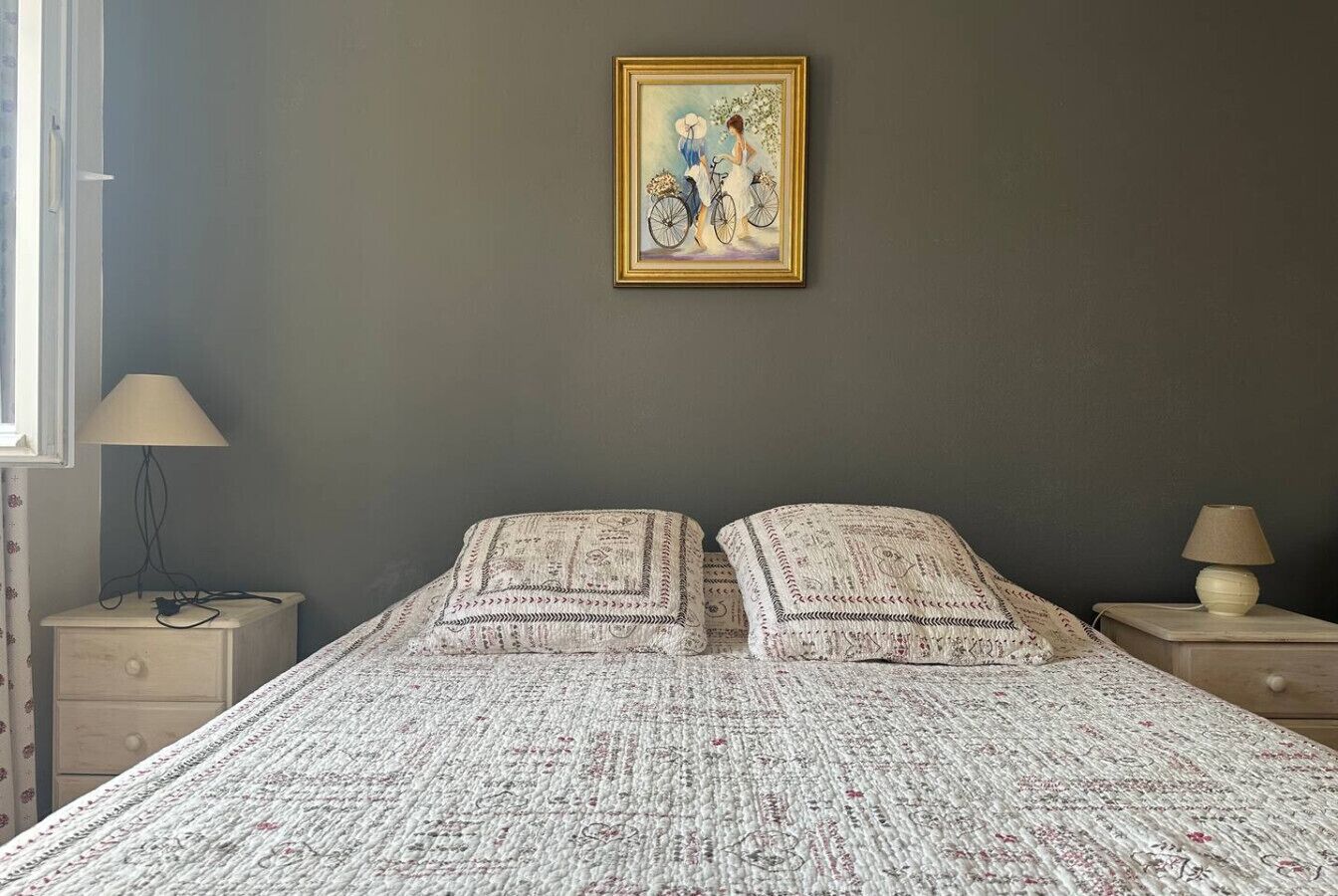 A bedroom with a bed, two pillows, a nightstand, a lamp, and a framed picture on the wall.