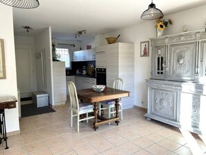 Ein Essbereich mit einem Holztisch und Stühlen, einem weißen Schrank mit dekorativen Schnitzereien und einem Fliesenboden.