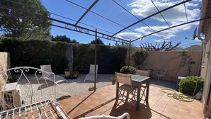 Un patio con una mesa y sillas de metal, una silla de metal blanco y una estructura de pérgola.