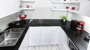 A kitchen with a black countertop, white cabinets, a stainless steel sink, and red and white appliances. - Historic and Stylish Apt at Calle Fortaleza! (San Juan)