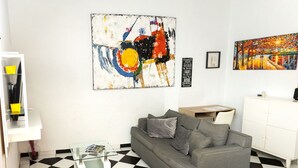 A living room with a checkered floor, a grey sofa, yellow armchairs, and two paintings on the wall. - Historic and Stylish Apt at Calle Fortaleza! (San Juan)
