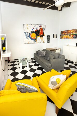 A living room with a checkered floor, a grey sofa, yellow armchairs, and two paintings on the wall. - Historic and Stylish Apt at Calle Fortaleza! (San Juan)