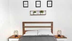A neatly made bed with a grey blanket, two bedside tables with geometric lamps, a wooden headboard, and three framed signs on the wall. - Historic and Stylish Apt at Calle Fortaleza! (San Juan)