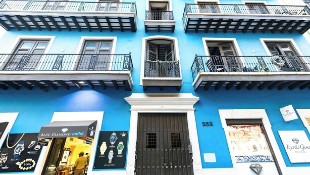 A blue building with balconies, a shop named "Blue Diamond Outlet," and a sign for "Exotic Gems Boutique." - Historic and Stylish Apt at Calle Fortaleza! (San Juan)