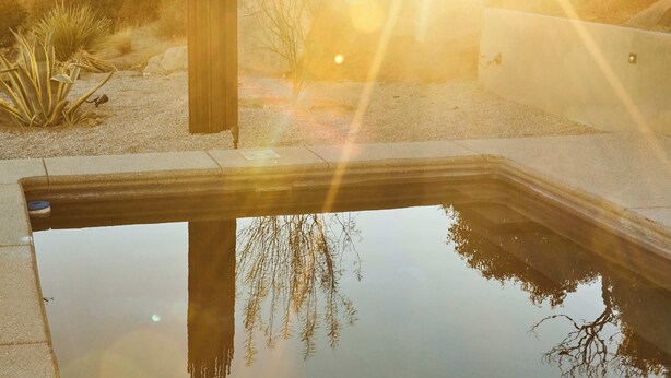 Paisaje desértico con un estanque reflectante, una estructura de madera y vegetación escasa.
