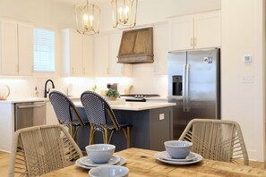 A modern kitchen with white cabinetry, a stainless steel refrigerator, and a dining area with a wooden table and wicker chairs. - "Sippin on Savannah Square" by OVR (Oxford)