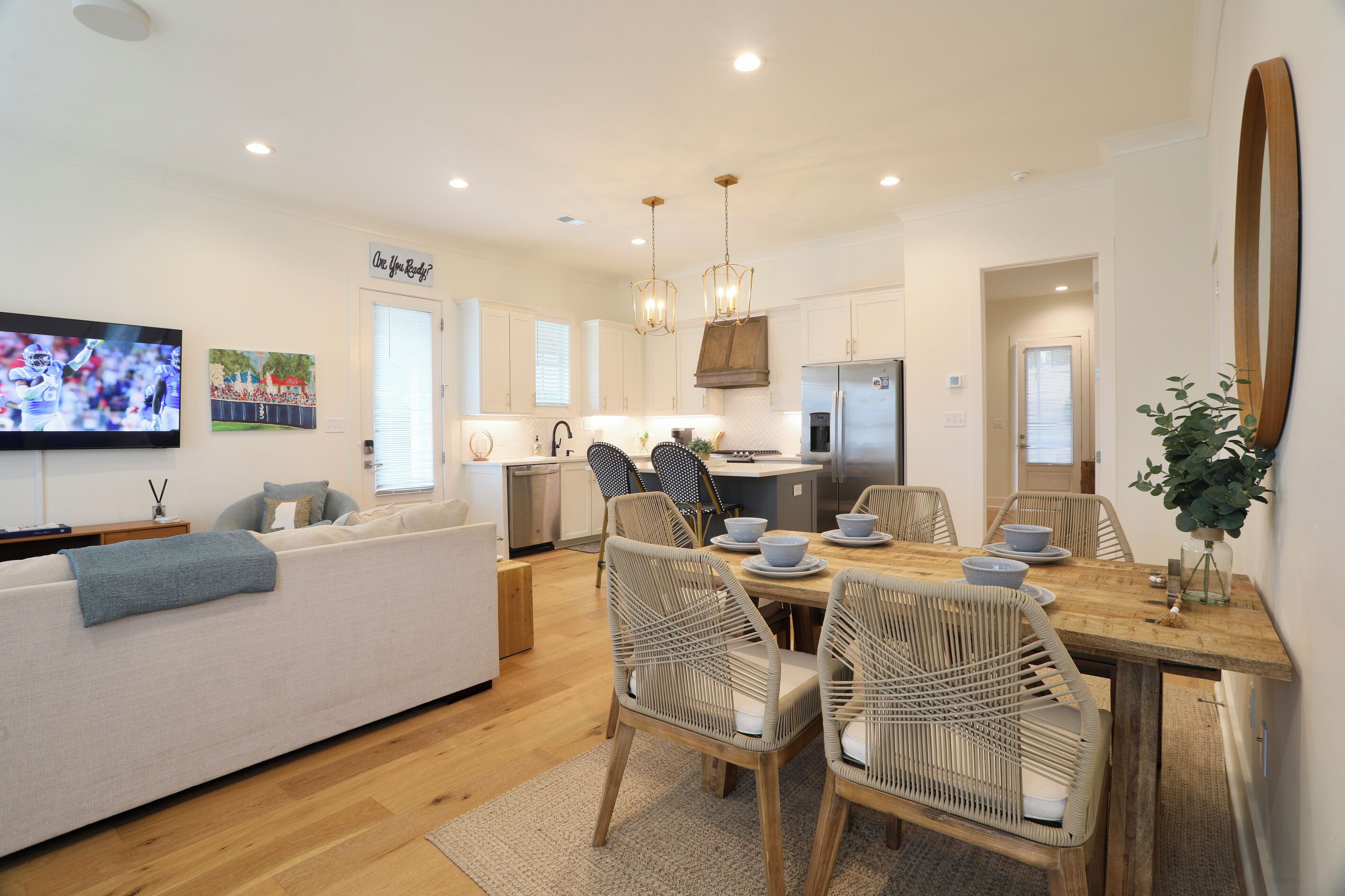 A modern kitchen with white cabinets, a stainless steel refrigerator, and a dining area with wicker chairs and a wooden table.