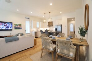 A modern kitchen with white cabinets, a stainless steel refrigerator, and a dining area with wicker chairs and a wooden table. - "Sippin on Savannah Square" by OVR (Oxford)