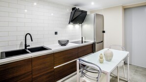 A modern kitchen with white subway tiles, a stainless steel refrigerator, a black range hood, a sink, and a dining table with chairs. - THE LYNX KONITSA (Konitsa)