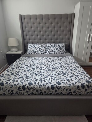 Un lit doté d’une tête de lit capitonnée, d’une couvre-lit à motifs floraux et d’une table de chevet avec une lampe.