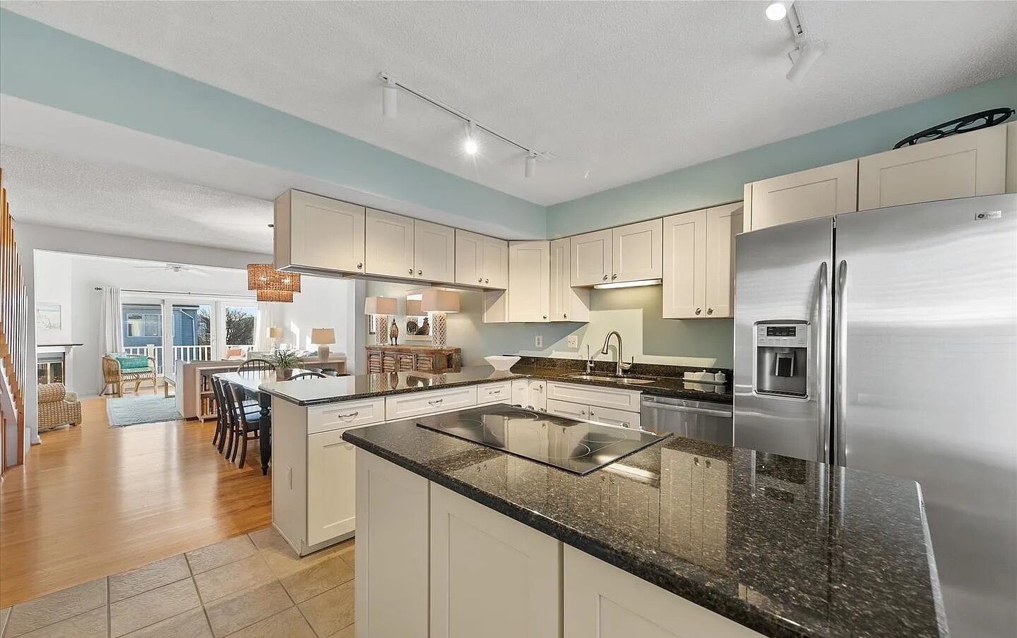 A modern kitchen with white cabinets, a stainless steel refrigerator, granite countertops, and a dining area with wooden chairs and a table.