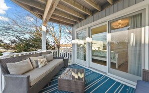 A covered outdoor seating area with a wicker sofa, a small table, and a blue-striped rug. - Pebble Paradise - Easy Walk to the Beach & Town (Bethany Beach)