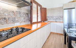 A kitchen with a gas stove, wooden cabinets, a stainless steel refrigerator, and patterned tile backsplash.
