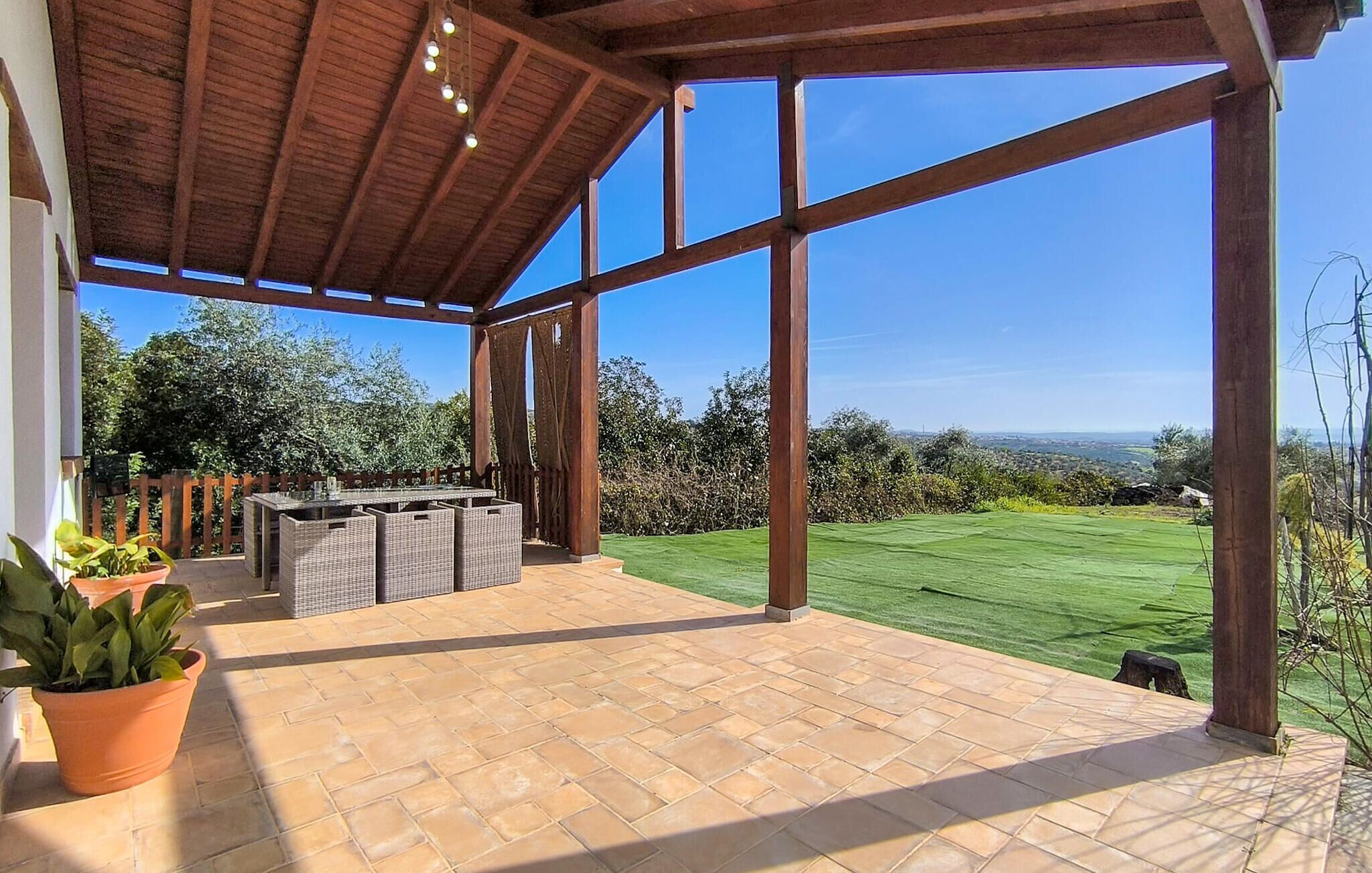 Une terrasse couverte offrant une vue sur une pelouse verdoyante et un paysage lointain.