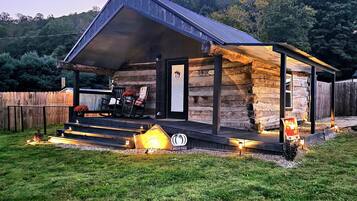 Une cabane rustique avec un porche, une pancarte de bienvenue et une autre qui annonce l’arrivée de l’automne.