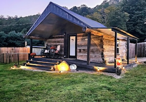 A rustic cabin with a porch, a welcome sign, and a 'Hello Fall' sign.